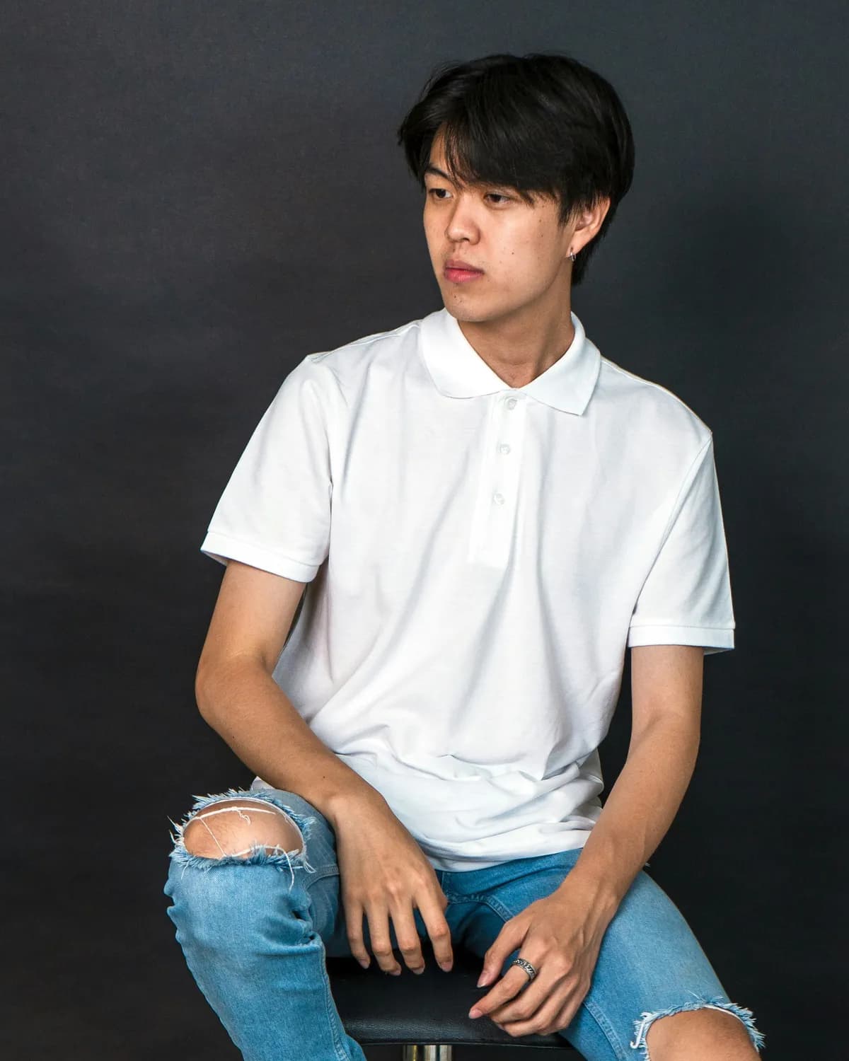 A man in a plain white polo sitting on a stool